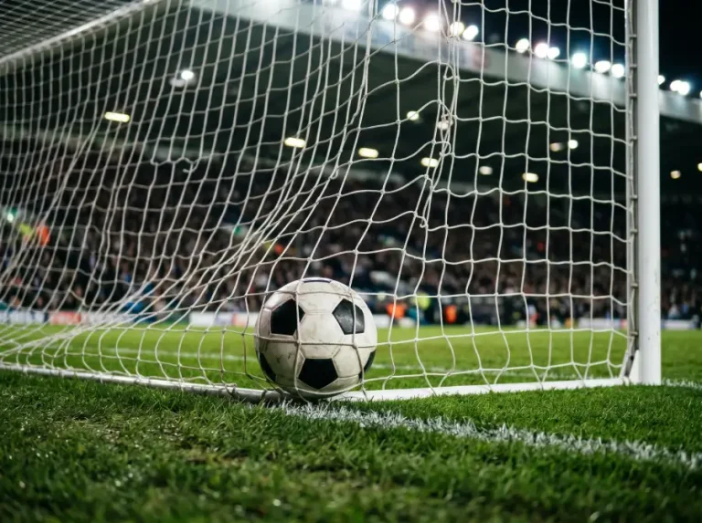 Balón de fútbol dentro de la portería con la red ondulando tras un gol, campo de hierba verde en primer plano