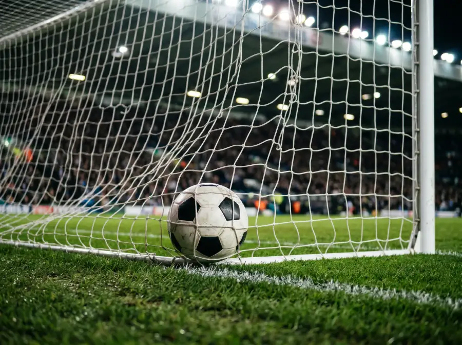 Balón de fútbol dentro de la portería con la red ondulando tras un gol, campo de hierba verde en primer plano